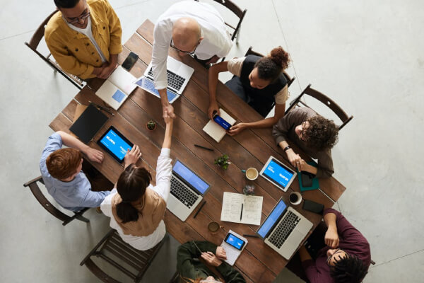 people sitting around a wooden table with laptops